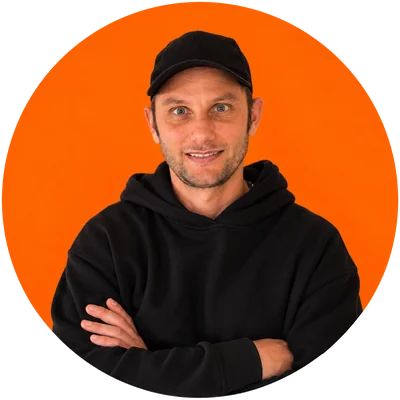 Nico Ciana, de gorra y buzo negro, con los brazos cruzados sobre fondo naranja